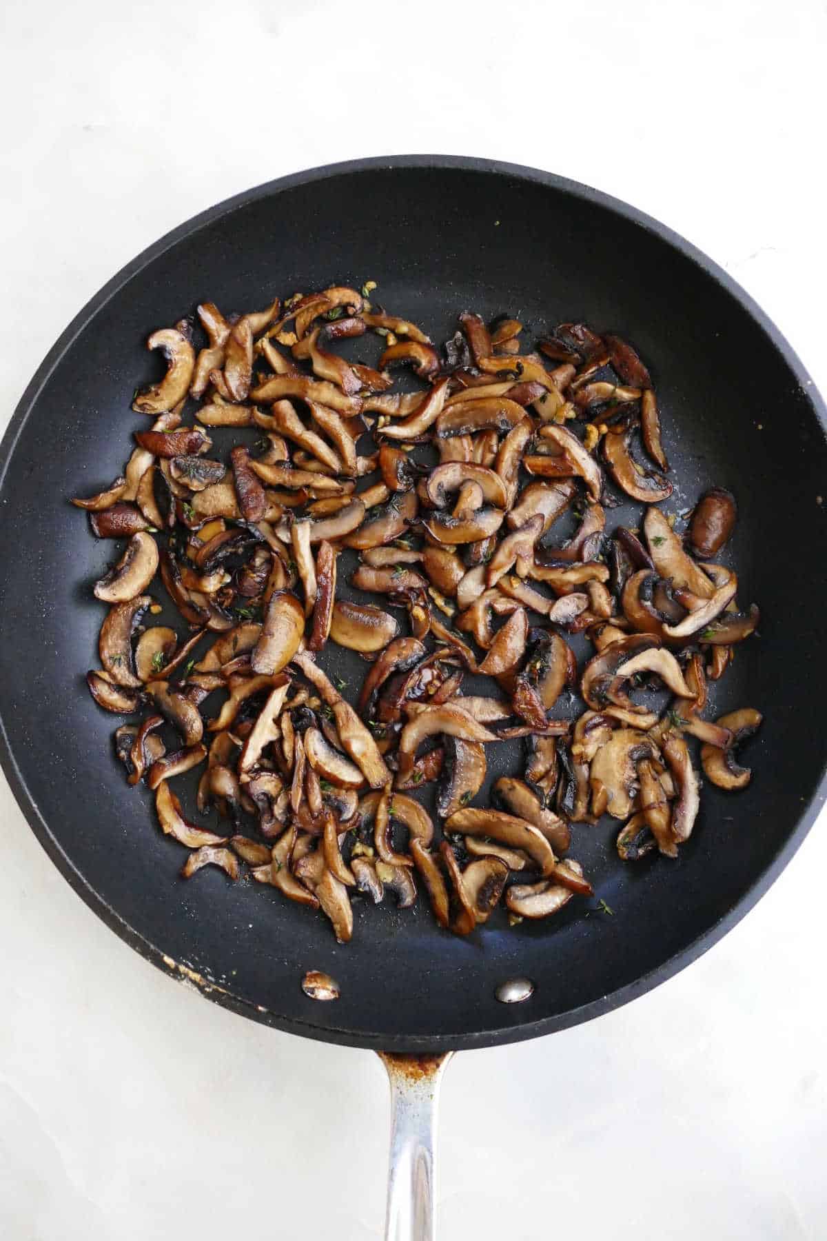 sliced cremini and shiitake mushrooms cooking in a large skillet with thyme
