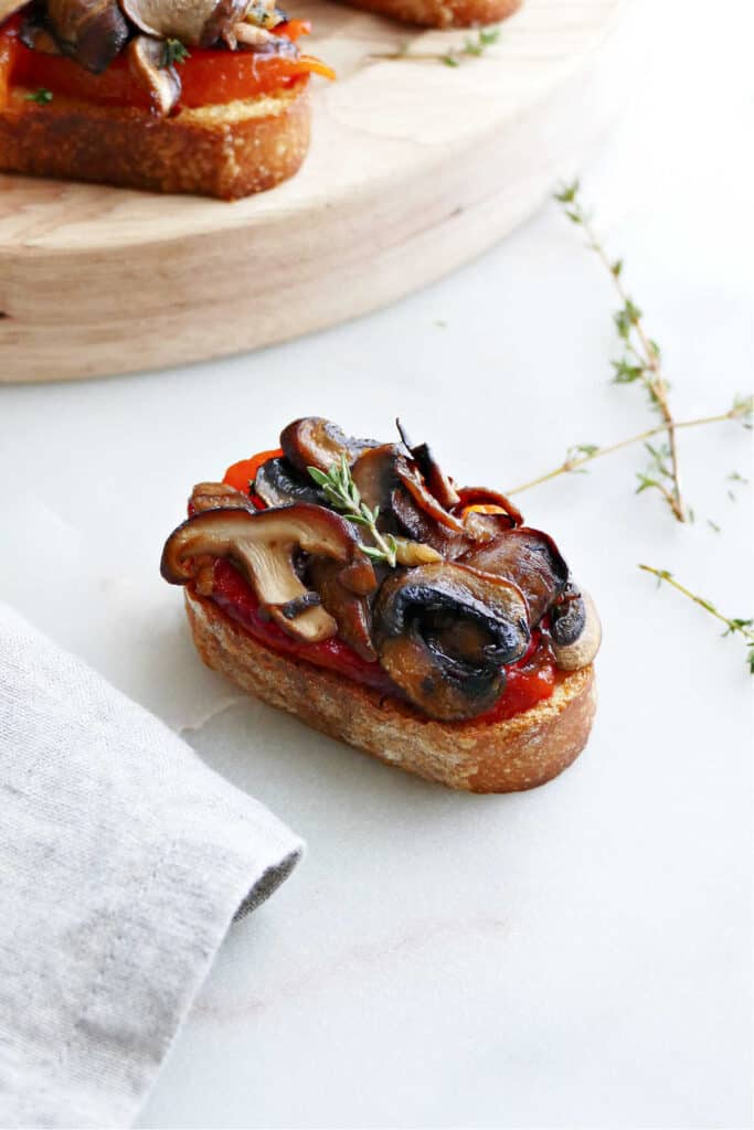 bruschetta with mushrooms and roasted peppers topped with a thyme sprig