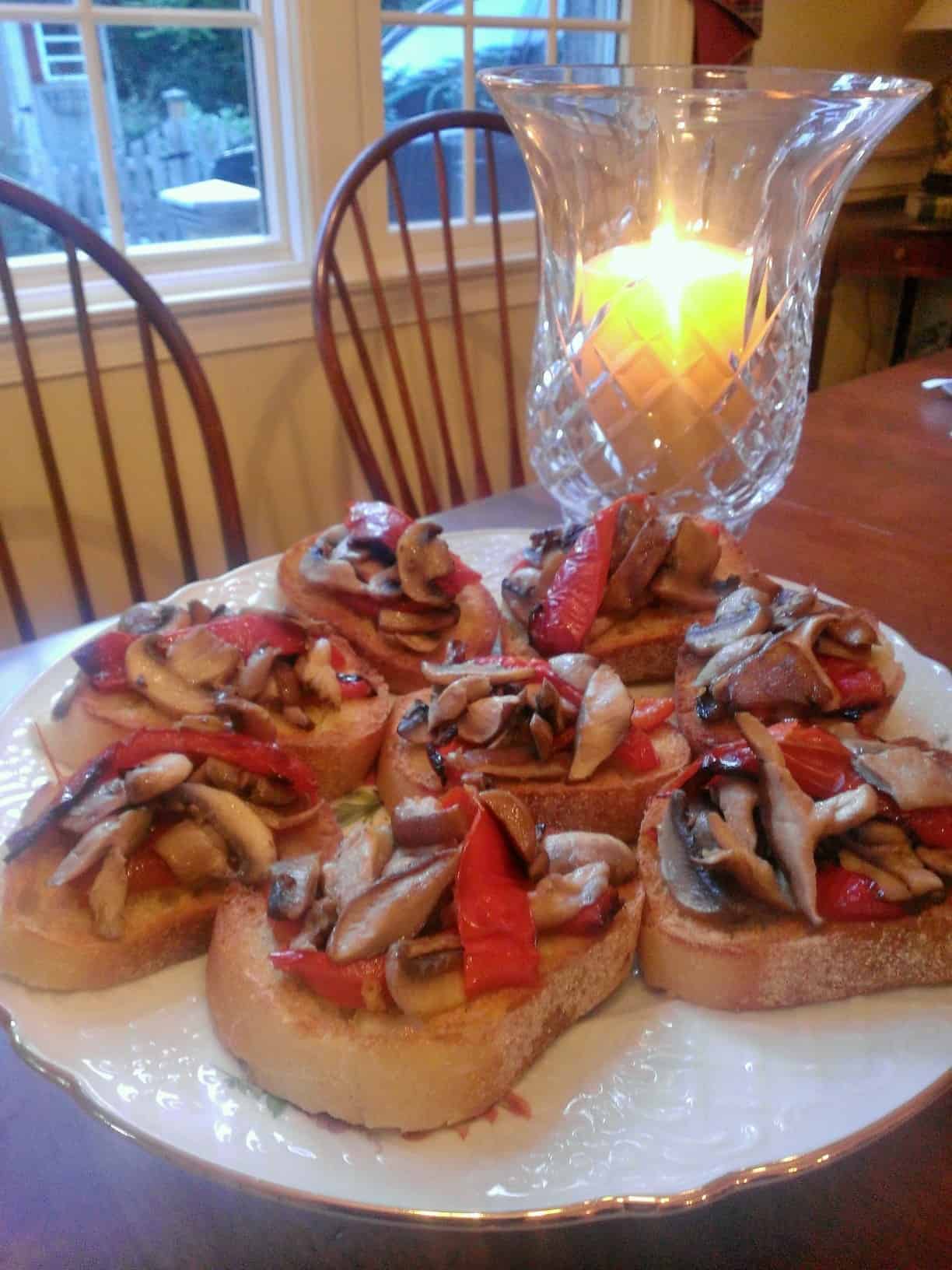 mushroom and pepper bruschetta on a serving platter next to a candle in a globe