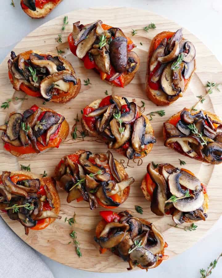 bruschetta with mushrooms and roasted peppers topped with thyme on a circular serving tray