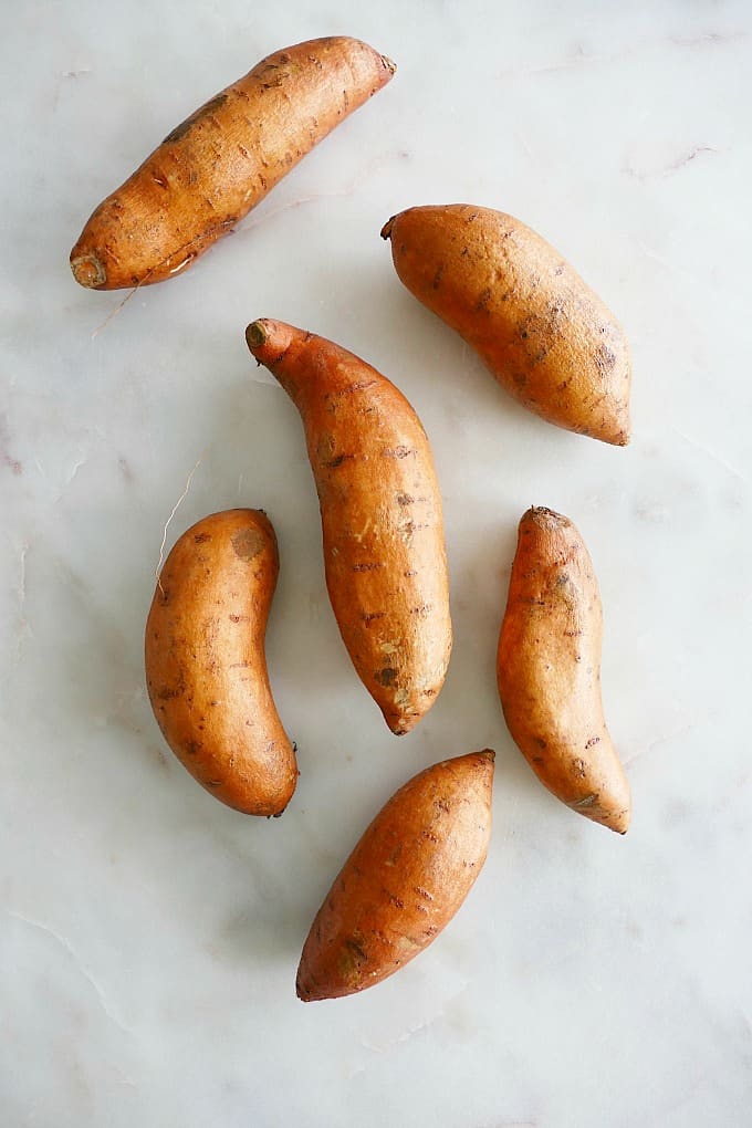 six sweet potatoes spread out next to each other on a white counter