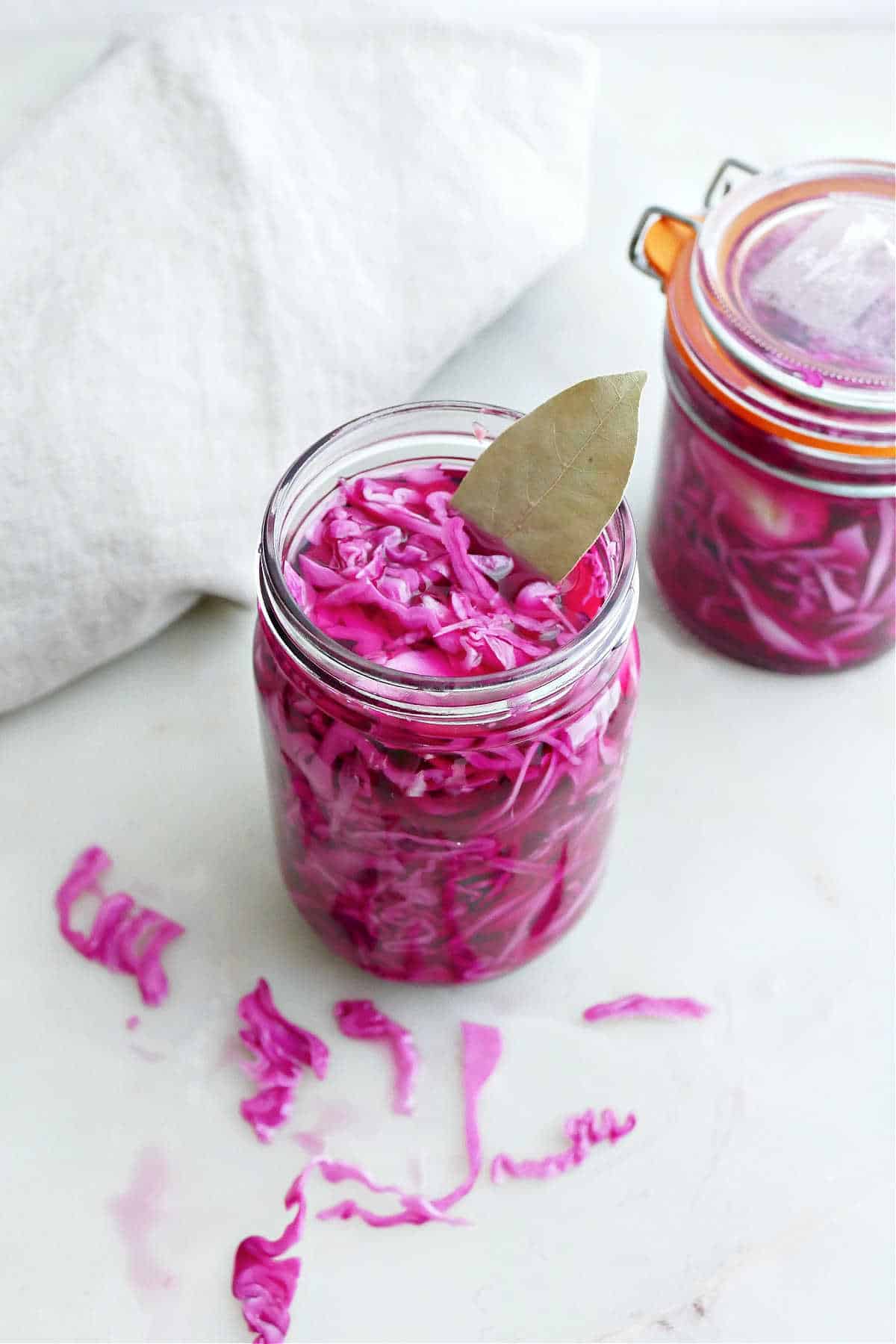 Pickled red cabbage in a glass jar with a bay leaf sticking out.