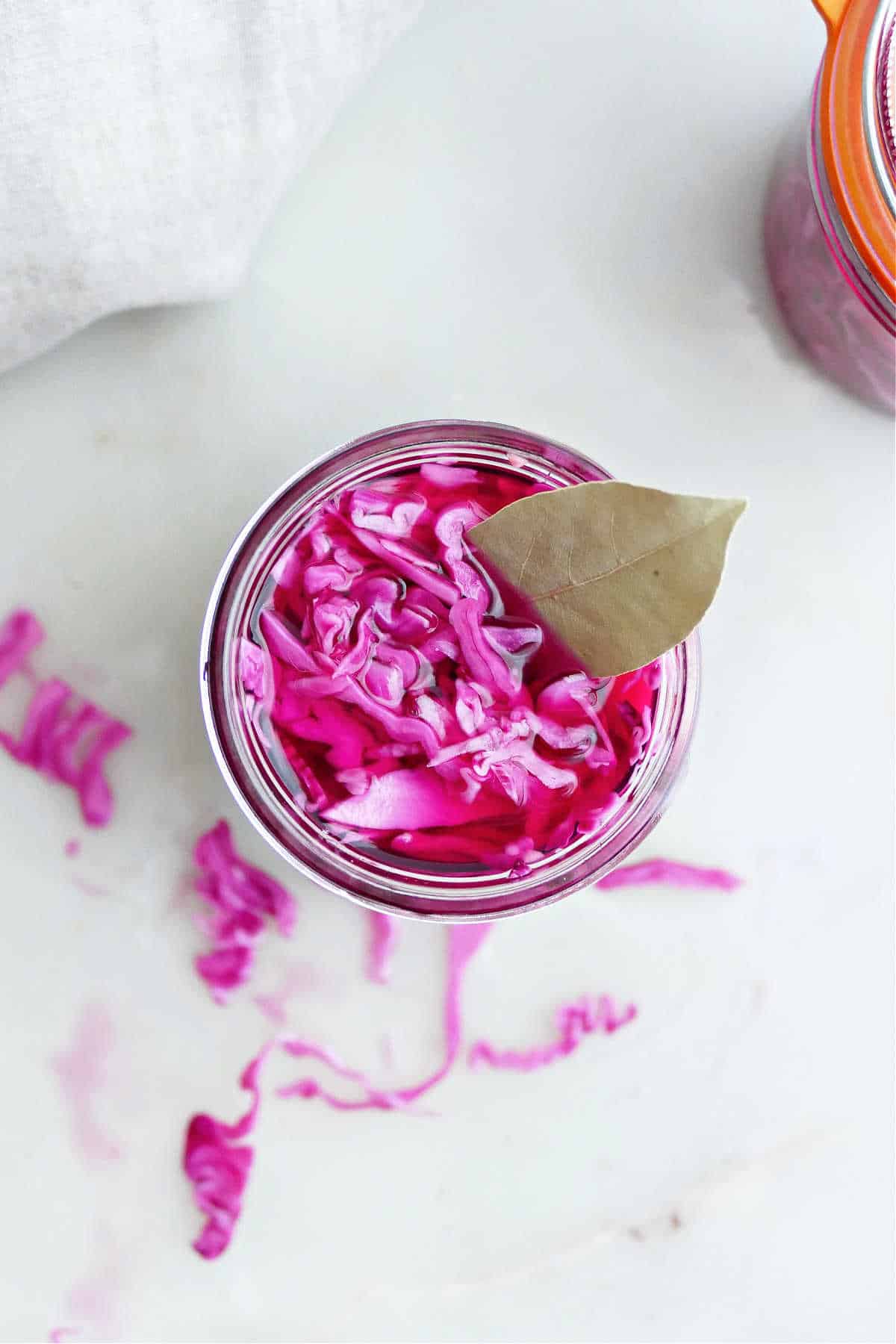 Marinated red cabbage with a bay leaf in a glass jar on a counter.