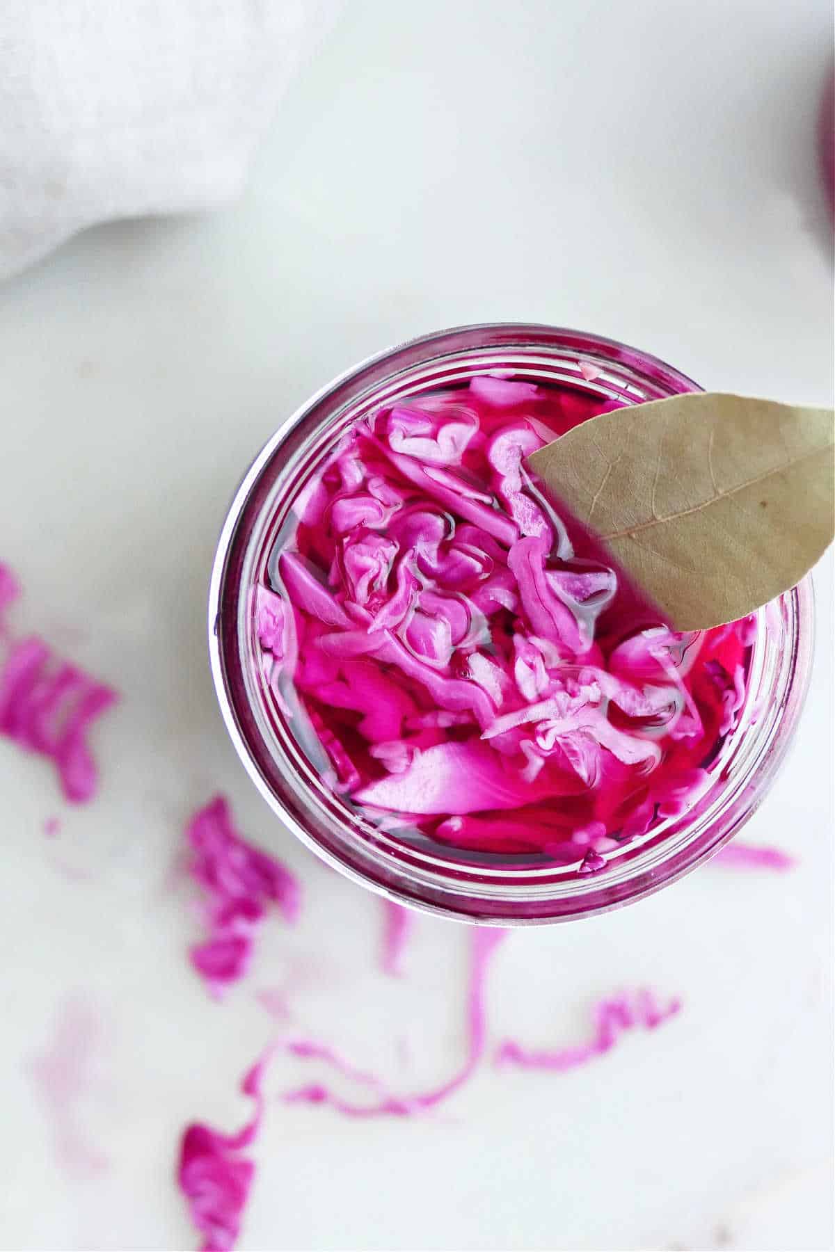 Quick pickled purple cabbage in a glass jar with a bay leaf.