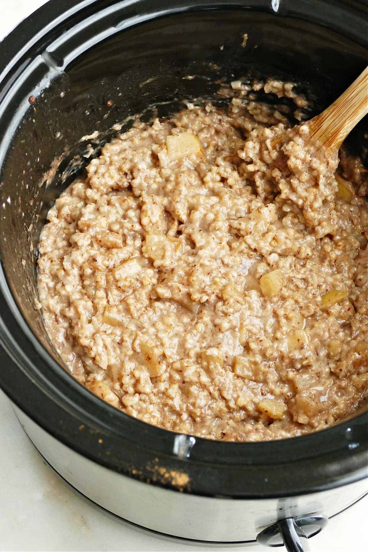 apple cinnamon oatmeal cooking in a crock pot with a wooden spoon