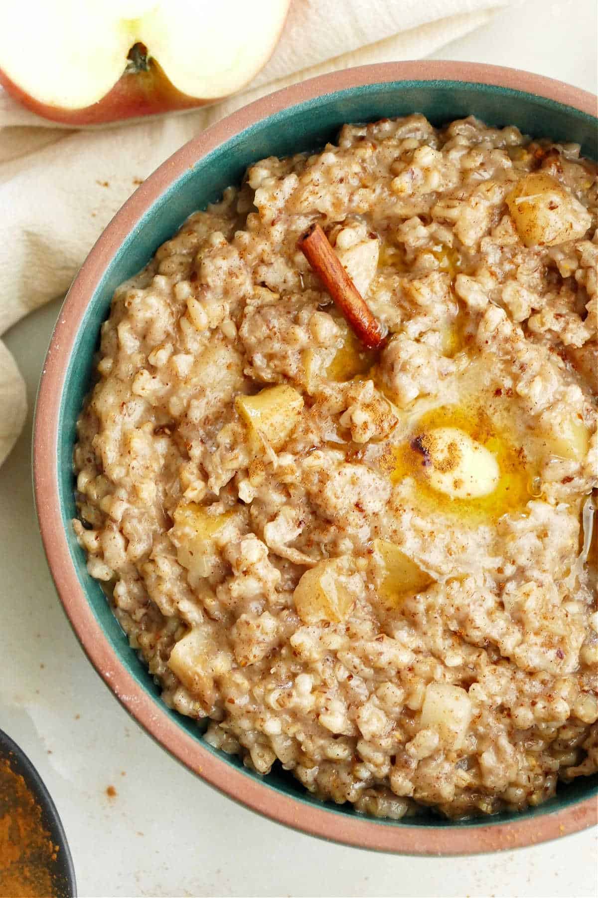 apple cinnamon oatmeal in a bowl with a cinnamon stick and butter