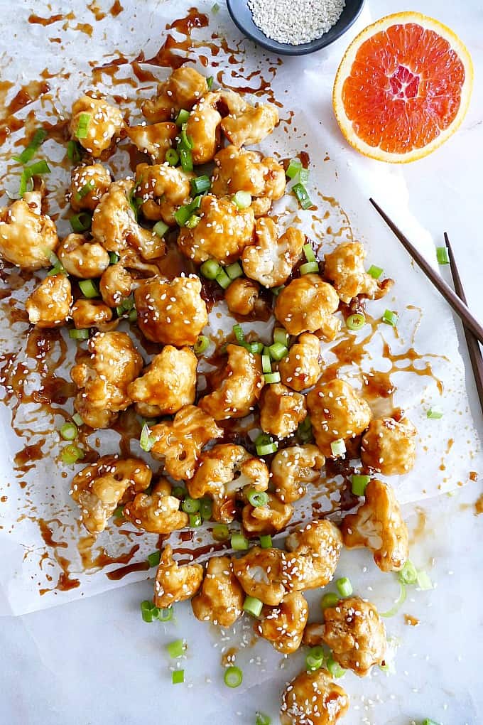 Baked sticky Orange Cauliflower on a white counter with chopped scallions and sesame seeds
