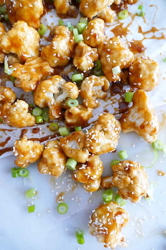 sticky orange cauliflower on a white background with chopped scallions and sesame seeds