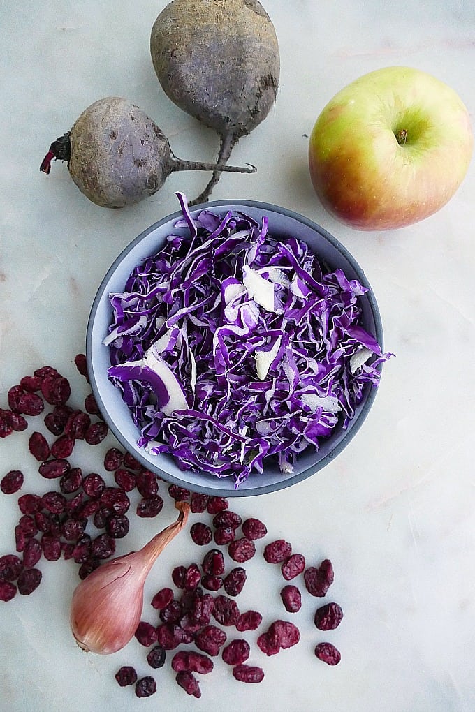 red cabbage, beets, apple, dried cranberries, and a shallot on a white counter