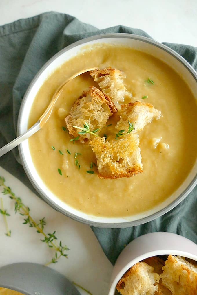 Vegan roasted parsnip and pear blender soup with croutons in a bowl with a spoon
