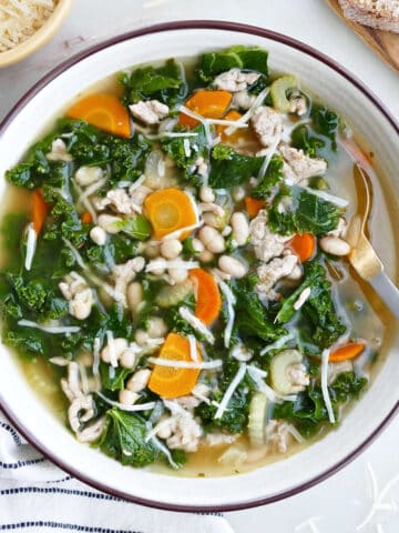 bowl of white bean, sausage, and kale soup topped with parmesan cheese