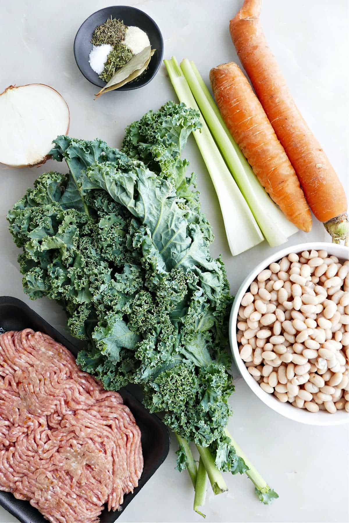 onion, spices, carrot, celery, white beans, kale, and sausage on a counter