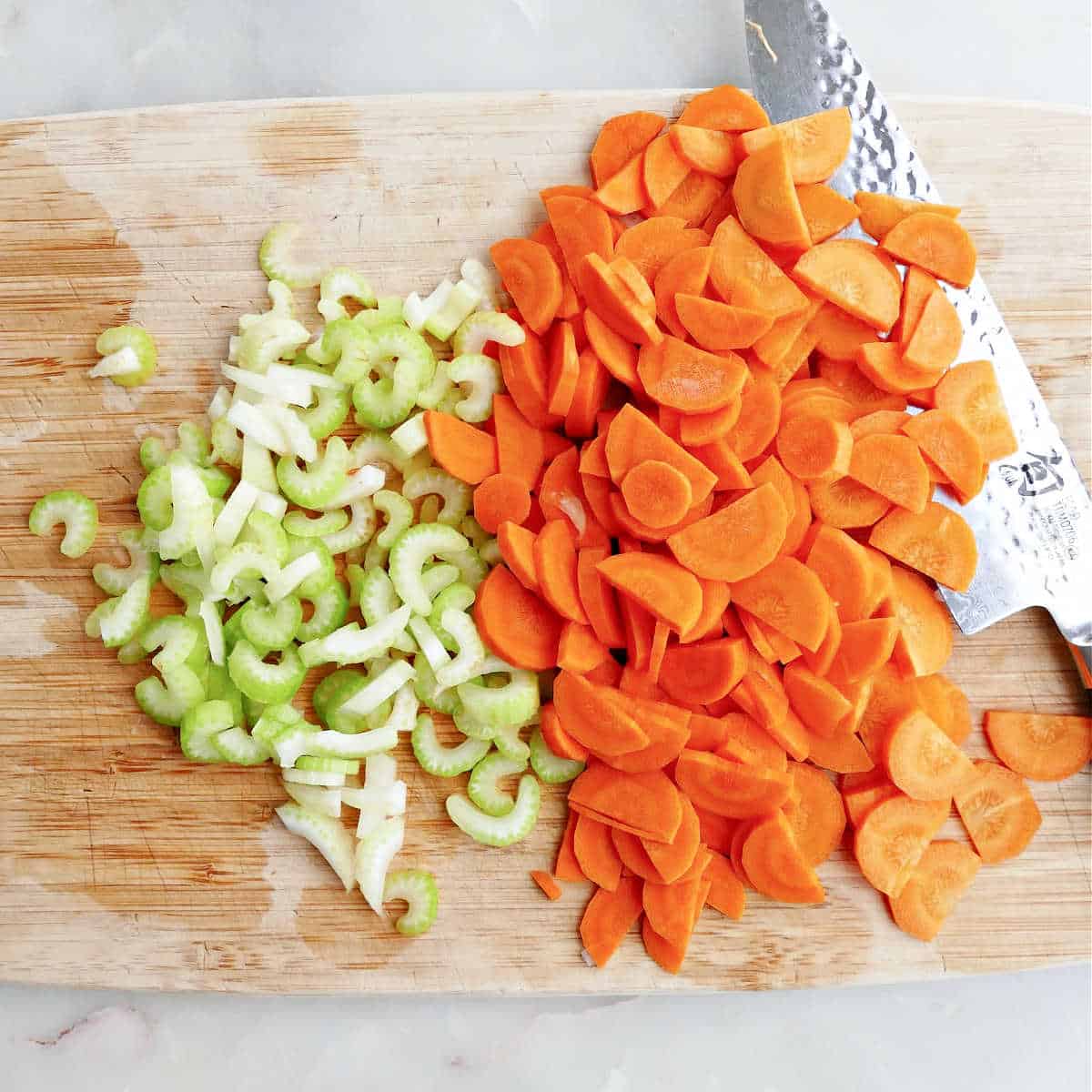 sliced celery and carrots on a cutting board with a chef's knife