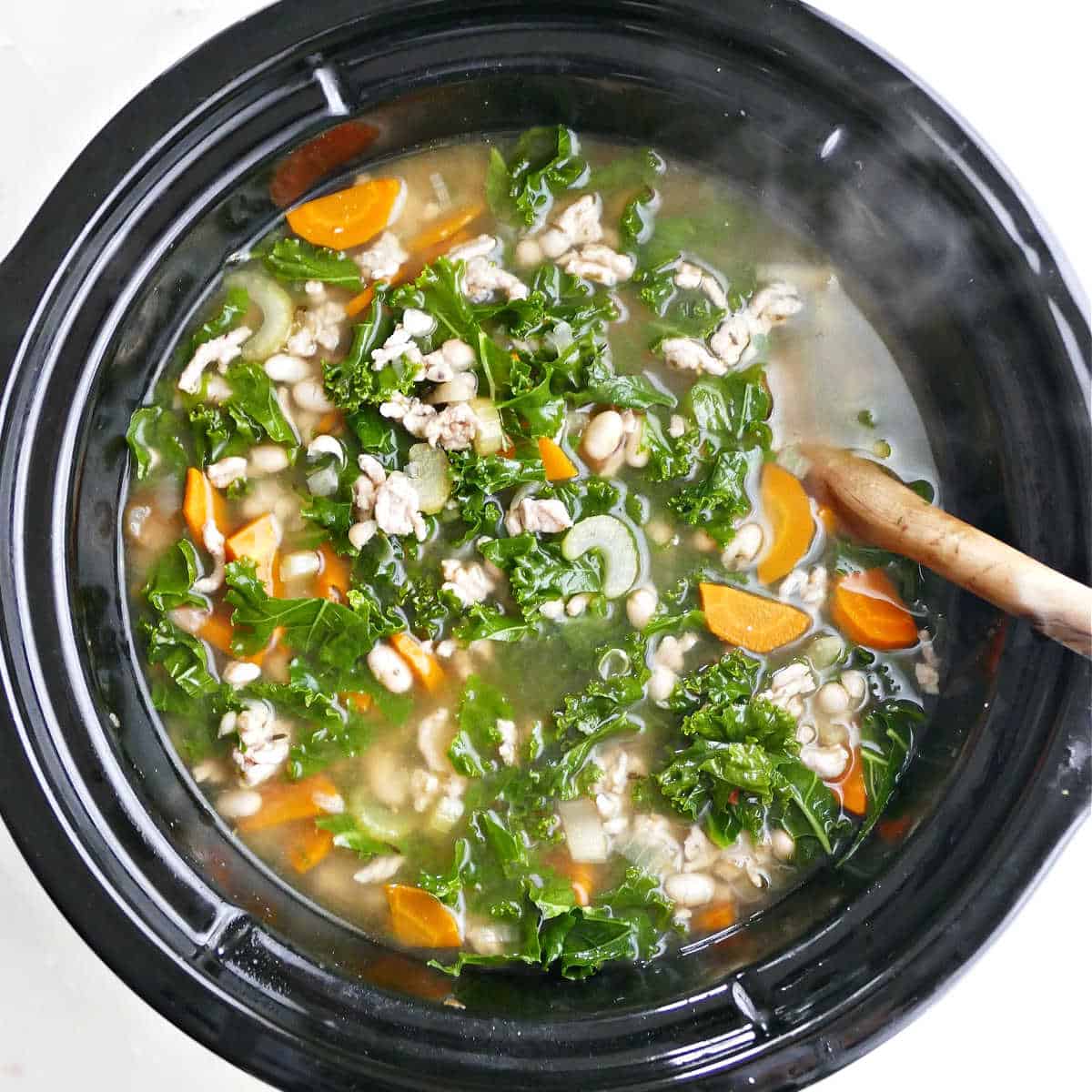 kale being mixed into soup in the slow cooker