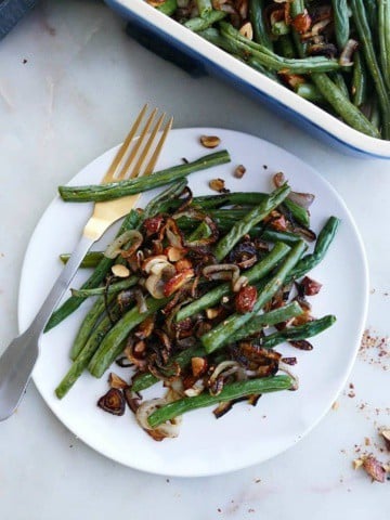 a serving of green bean casserole with almonds and shallots on a white plate