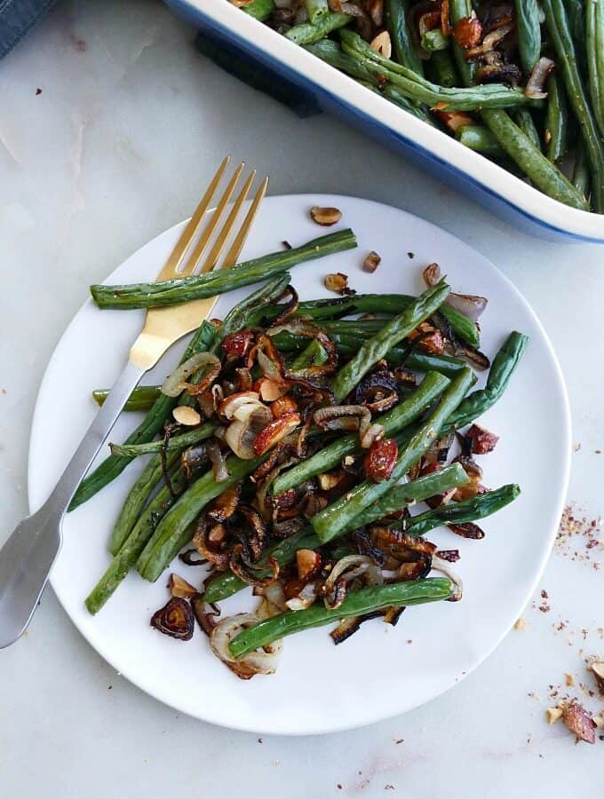 a serving of green bean casserole with almonds and shallots on a white plate