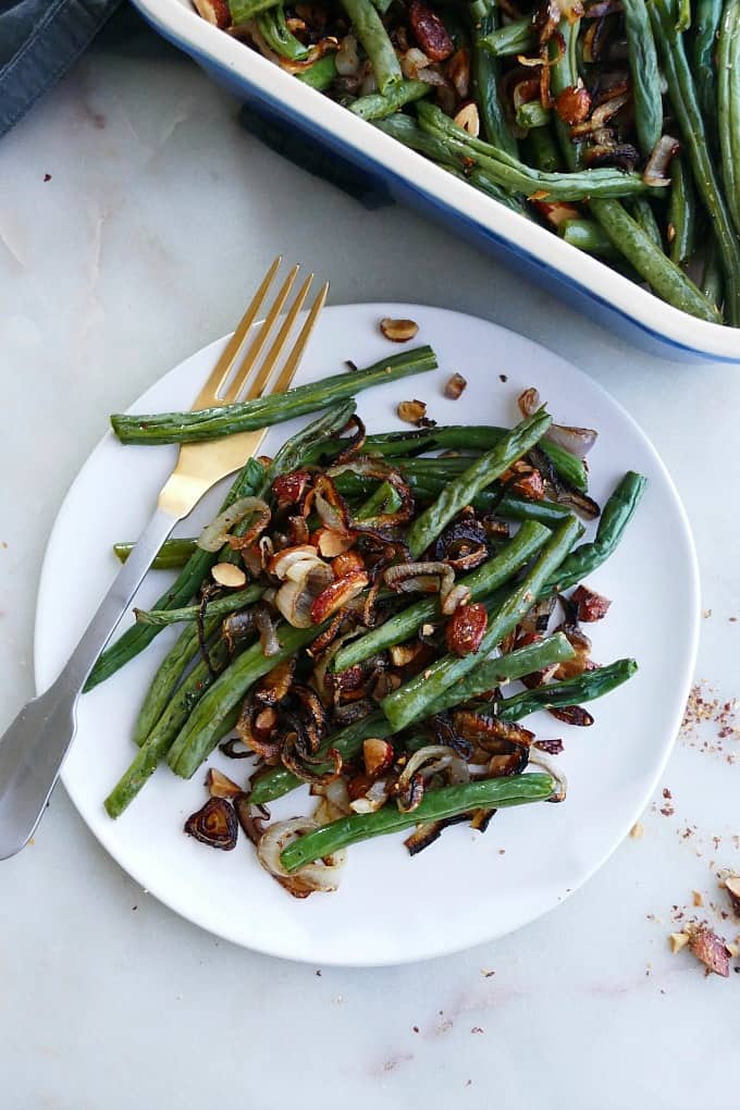 a serving of green bean casserole with almonds and shallots on a white plate