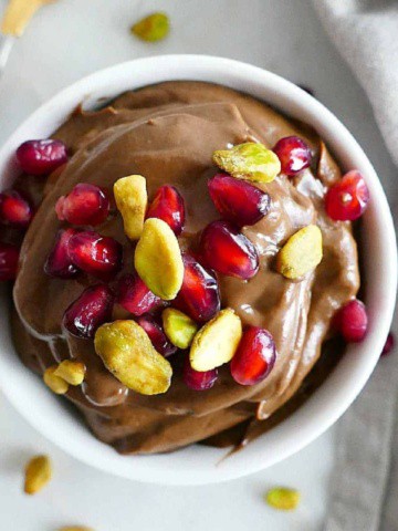 avocado chocolate mousse topped with pistachios and pomegranate arils in a serving bowl