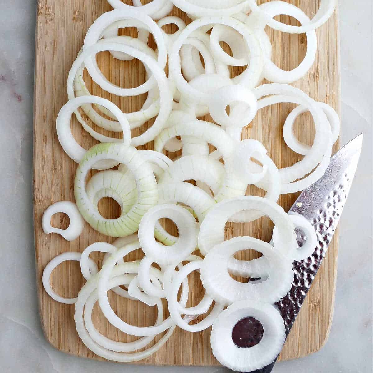 an onion sliced into rings on a bamboo cutting board on a counter