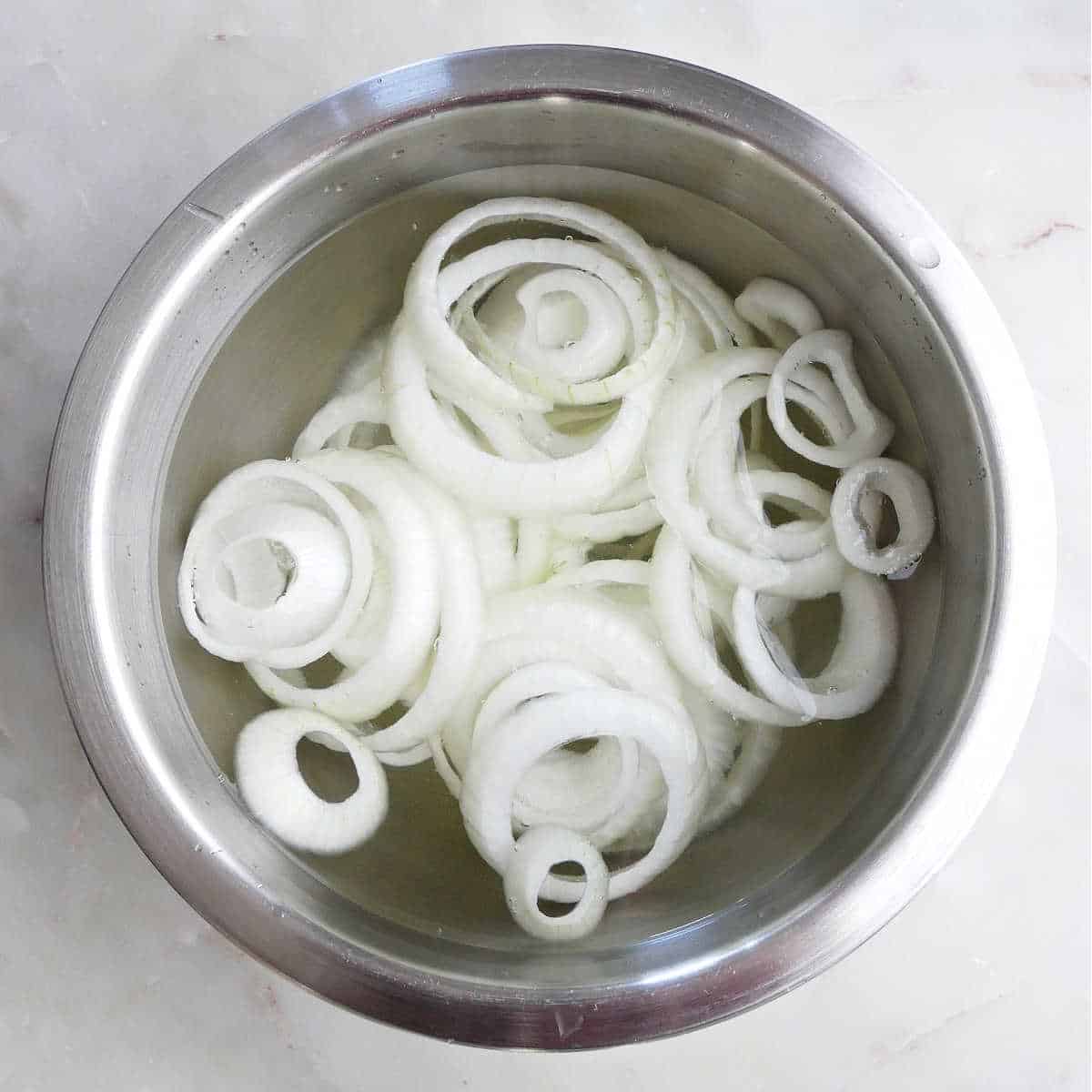 sliced onions in a large mixing bowl with water on a counter