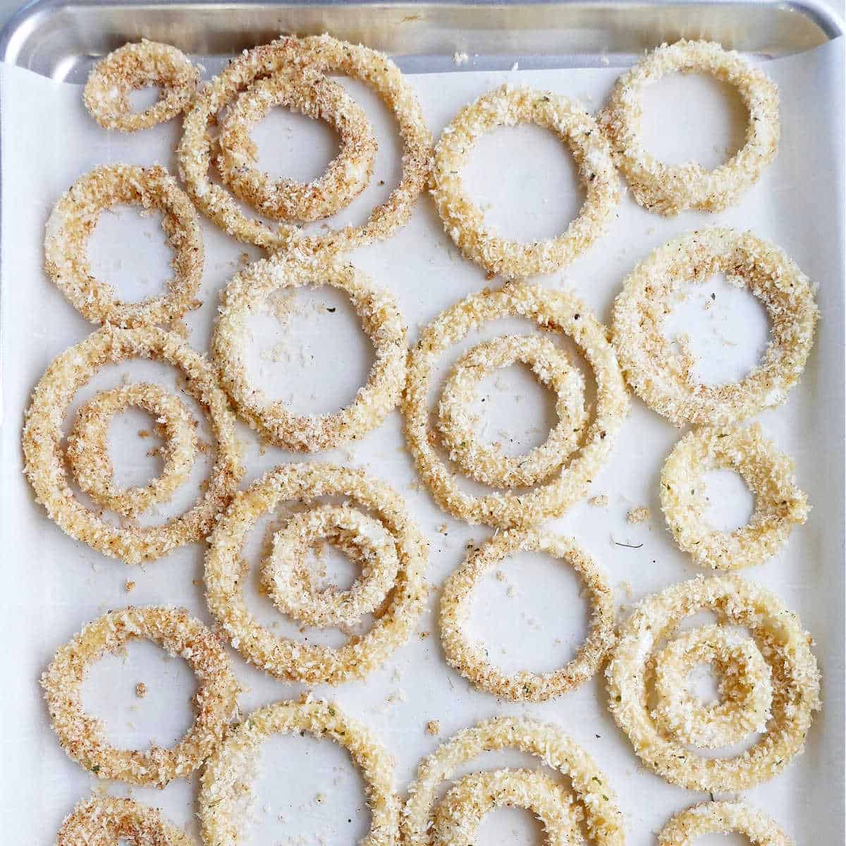 panko onion rings coated in breading on a lined baking sheet