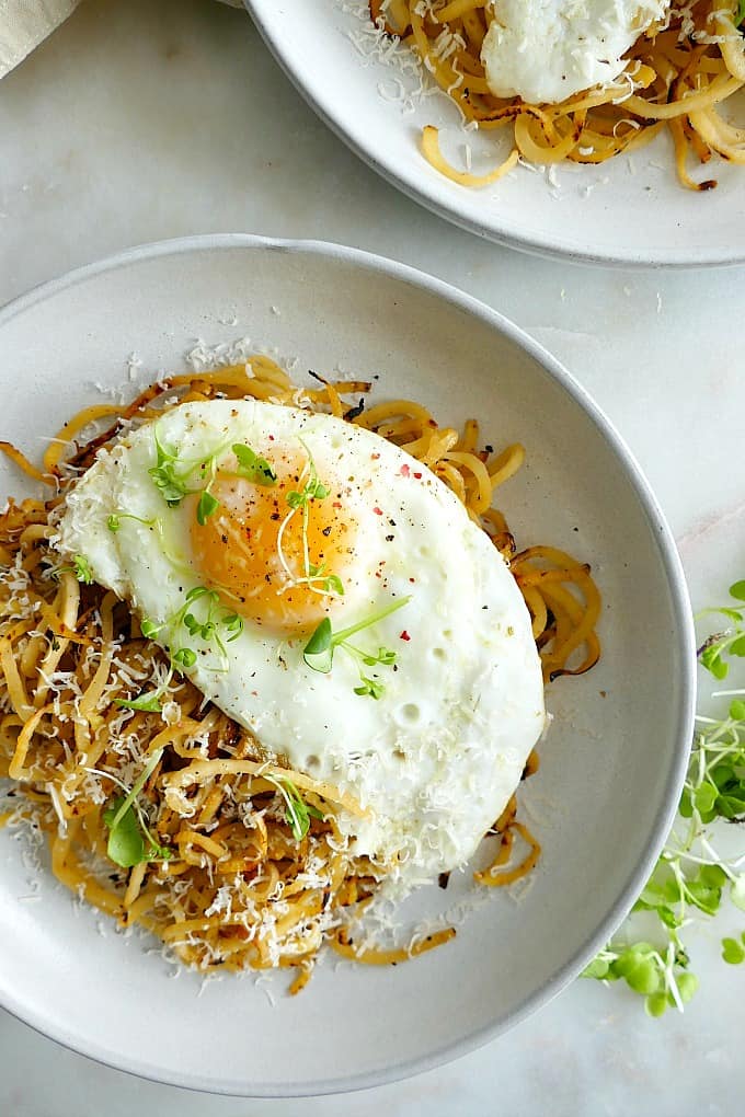 rutabaga noodles on a plate topped with an over easy egg, greens, and cheese