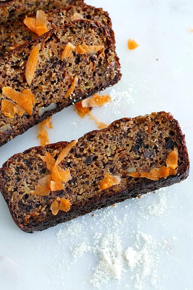 slice of carrot banana bread on a white counter with shredded carrots on top