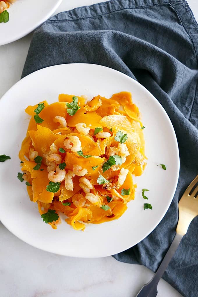 A plate of garlic lemon butternut squash noodles and shrimp next to a dark blue dish towel. 
