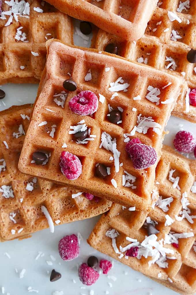 pink waffles on top of each other on a white counter topped with fruit and coconut