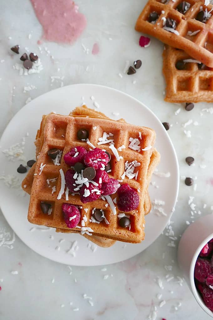 close up of a stack of pink waffles with raspberries and chocolate chips