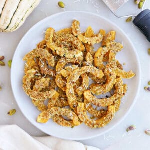 Parmesan delicata squash on a serving plate surrounded by ingredients.