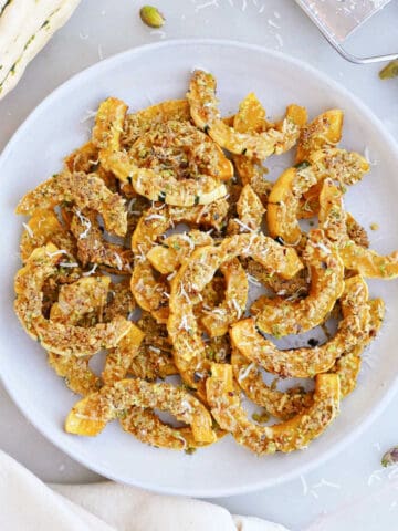 Parmesan delicata squash on a serving plate surrounded by ingredients.