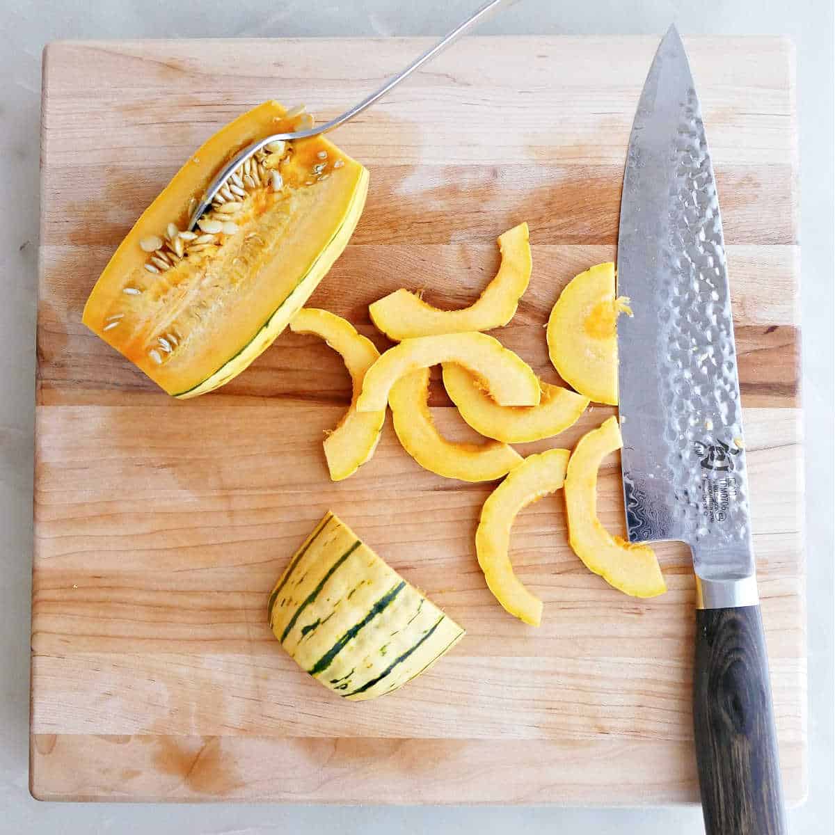 Delicata squash being prepared into slices on a cutting board.