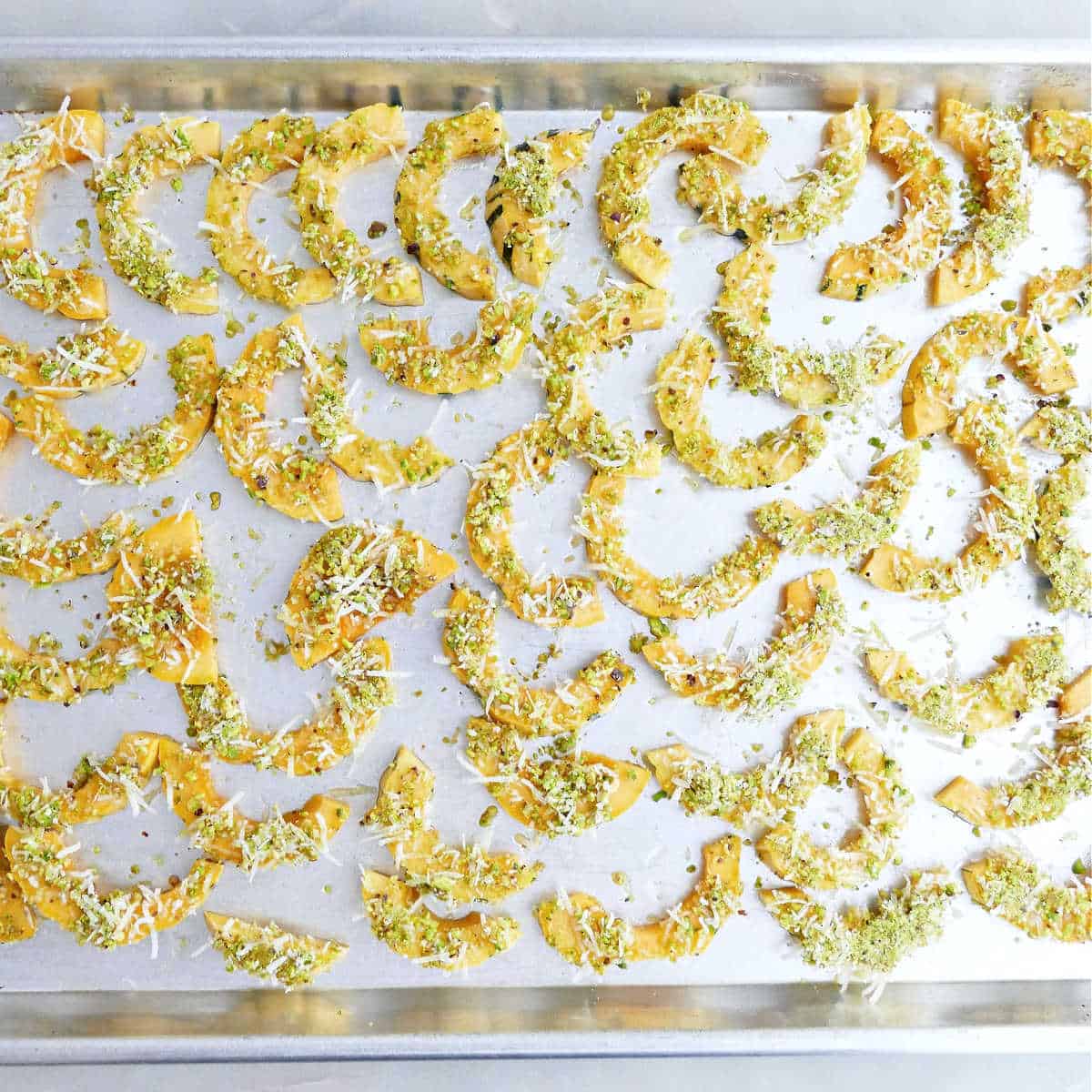 Parmesan pistachio delicata squash slices on a baking sheet before going in the oven.