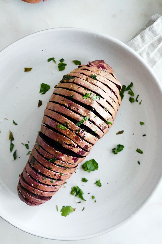 Hasselback Purple Sweet Potato topped with chopped parsley on a white plate