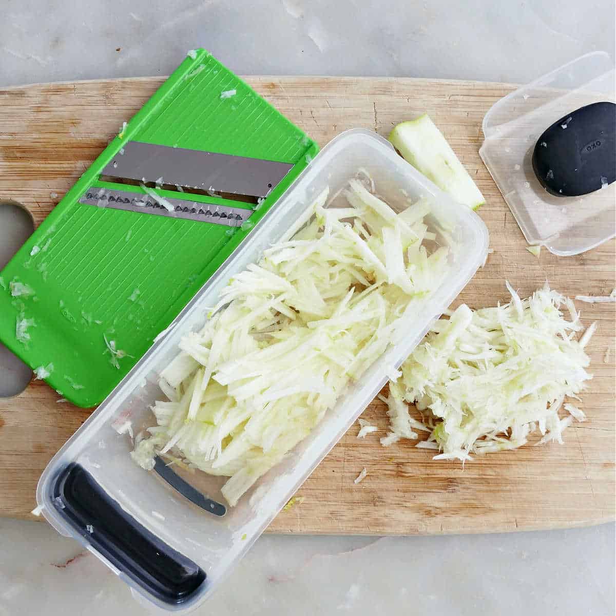 Shredded fennel in a grating container on a cutting board.