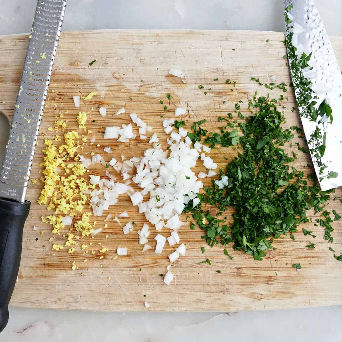 Chopped ginger, onion, and parsley on a cutting board.