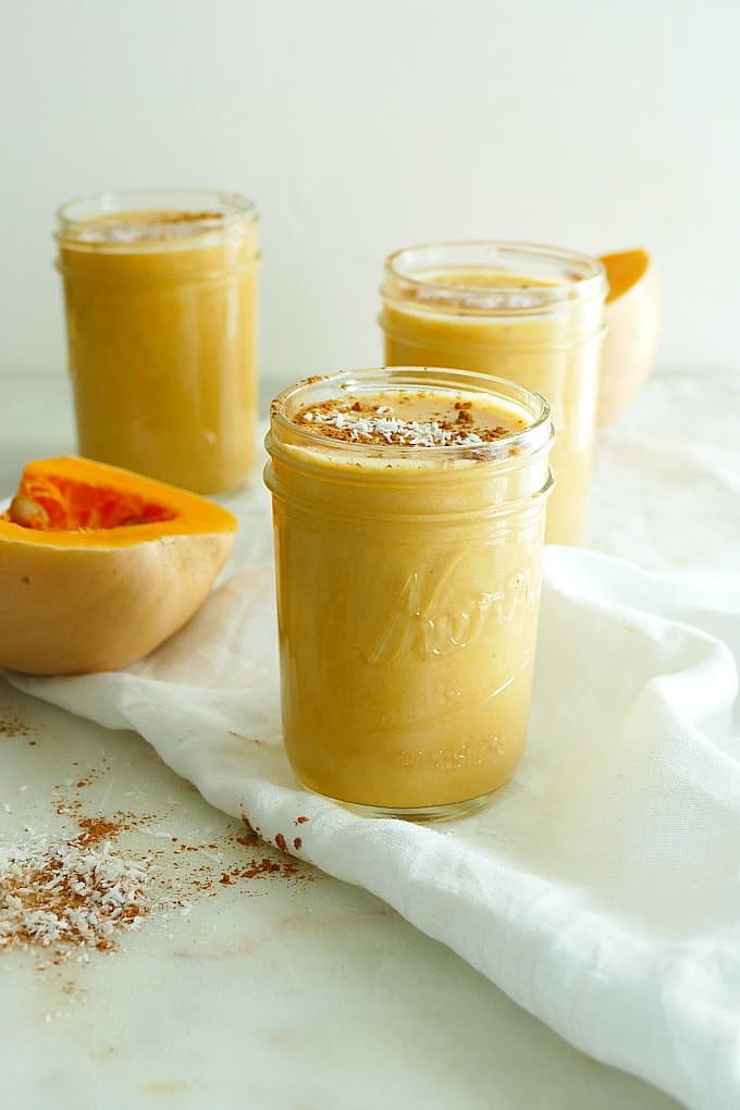 three glass jars with butternut squash smoothie on a white towel on a counter