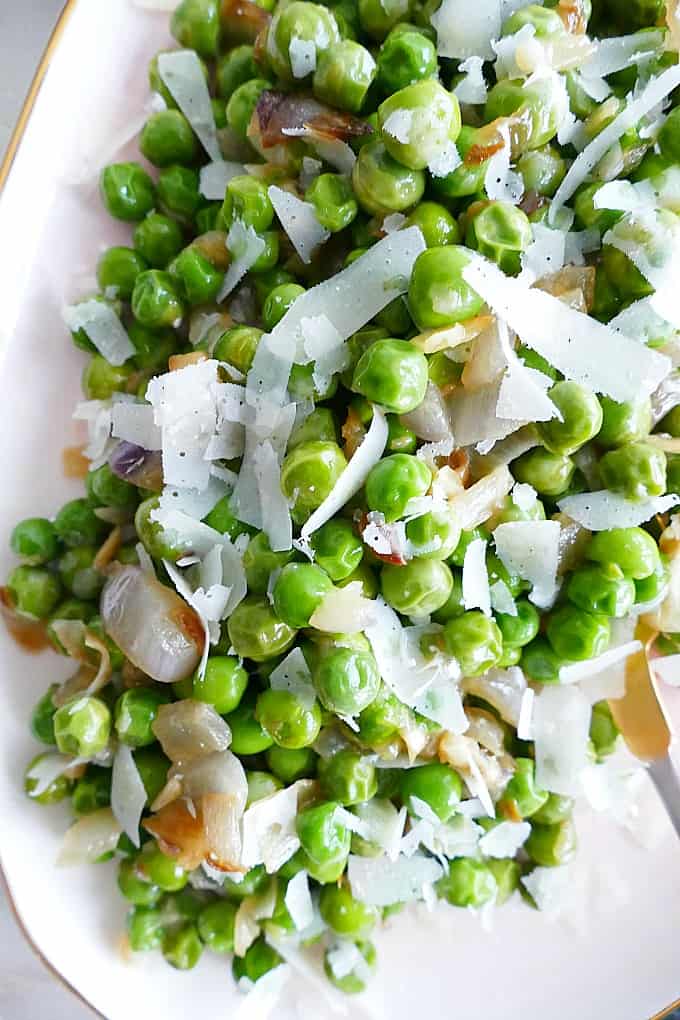 close up of parmesan peas with shallots on a pink serving tray