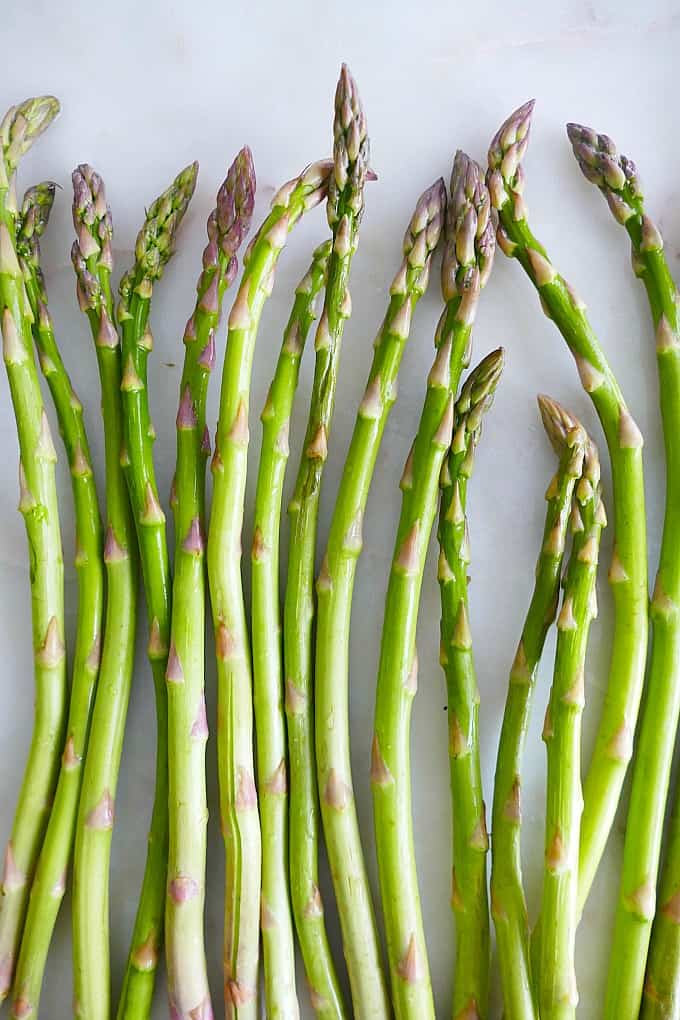 thin asparagus stalks spread out next to each other on a white marble counter