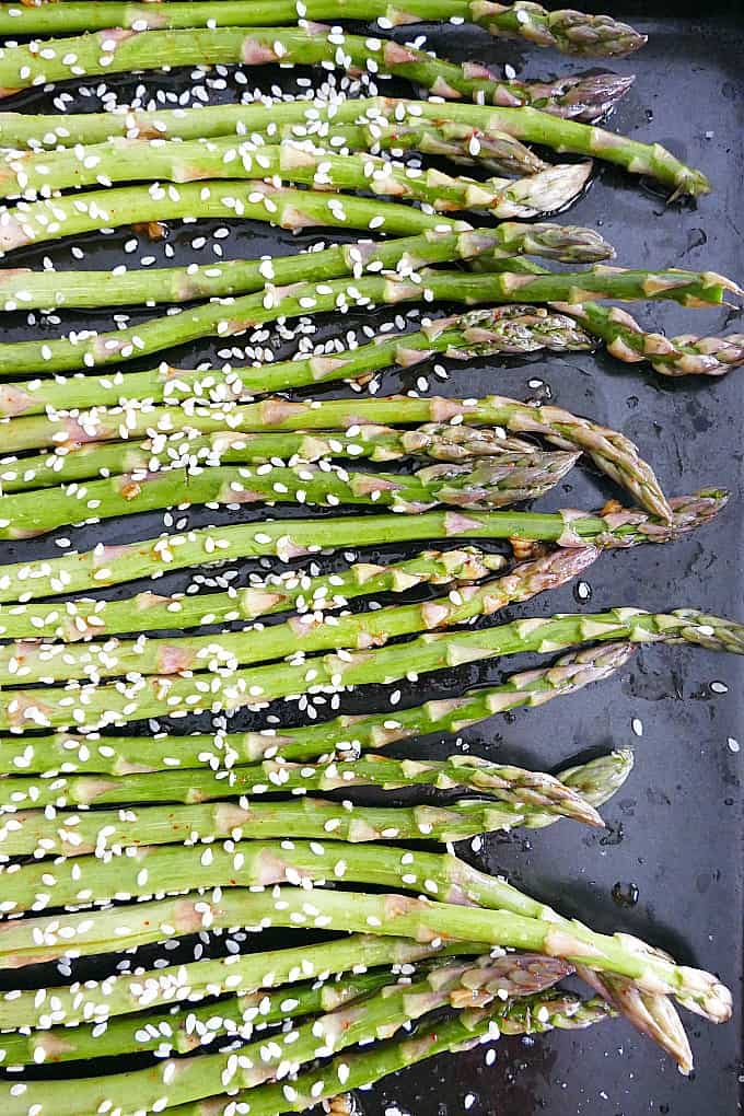 asparagus spears topped with sesame seeds on a baking sheet