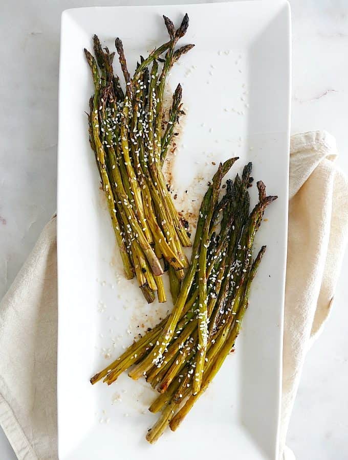 roasted sesame asparagus separated into two bunches on a white serving platter