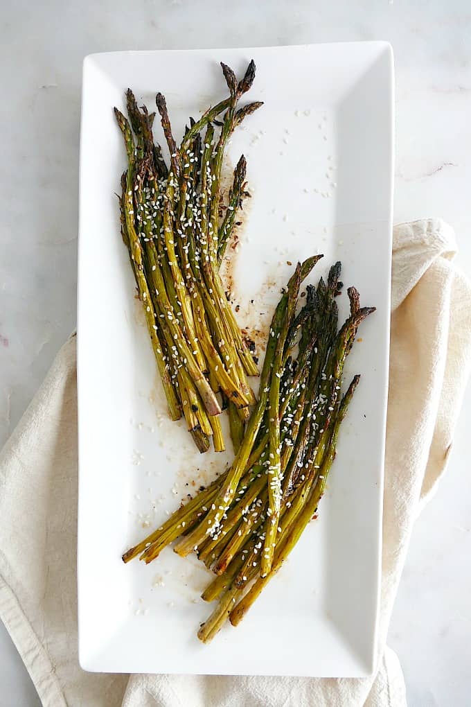 roasted sesame asparagus separated into two bunches on a white serving platter