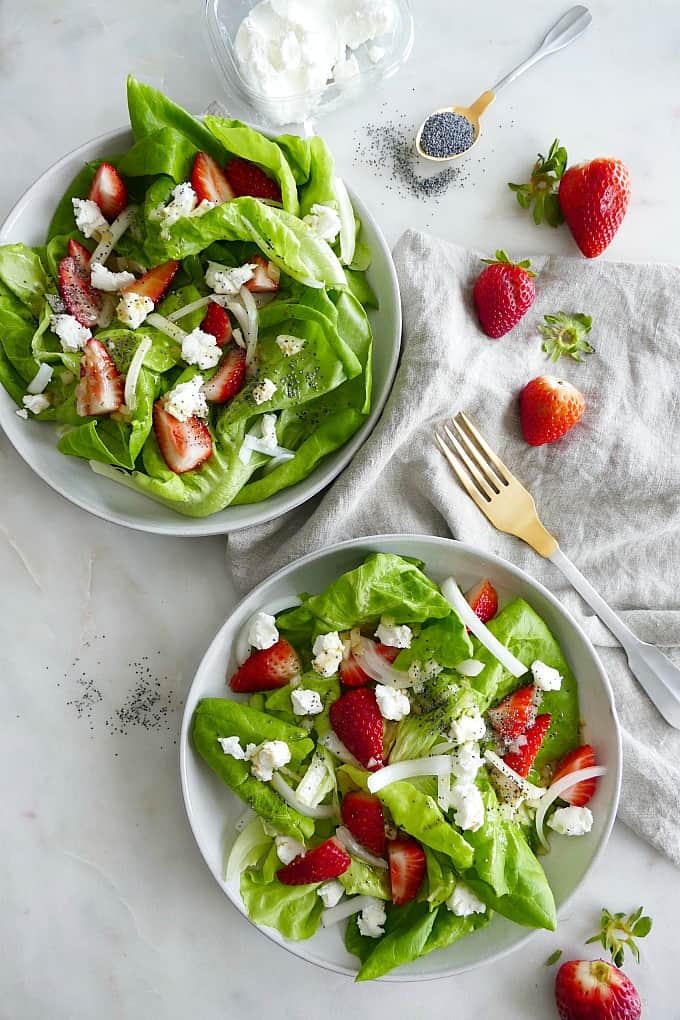 two plates with the finished salad on top of a gray napkins on a white counter