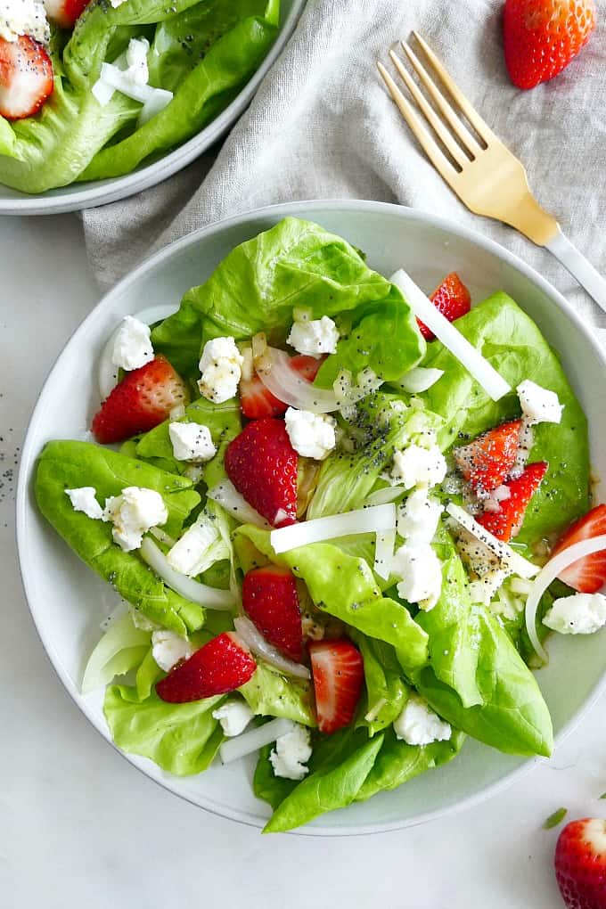 Butter Lettuce Strawberry Salad with goat cheese on a white plate on a counter