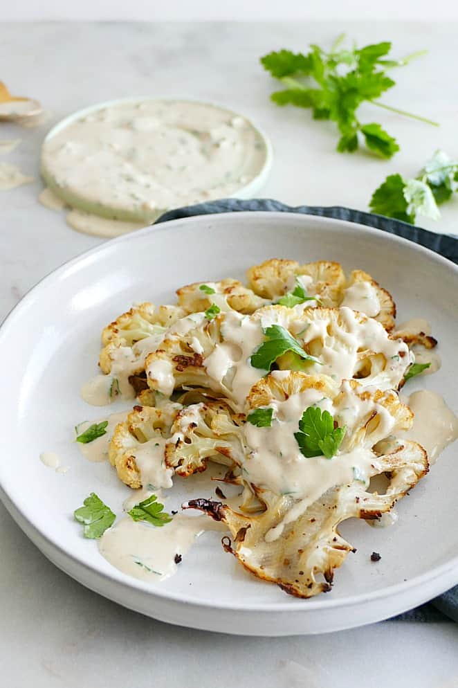 side view of three sliced cauliflower pieces on a white plate with tahini sauce