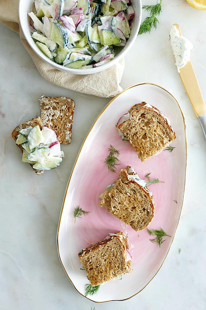 three mini cucumber sandwiches on a pink tray next to a bowl with filling