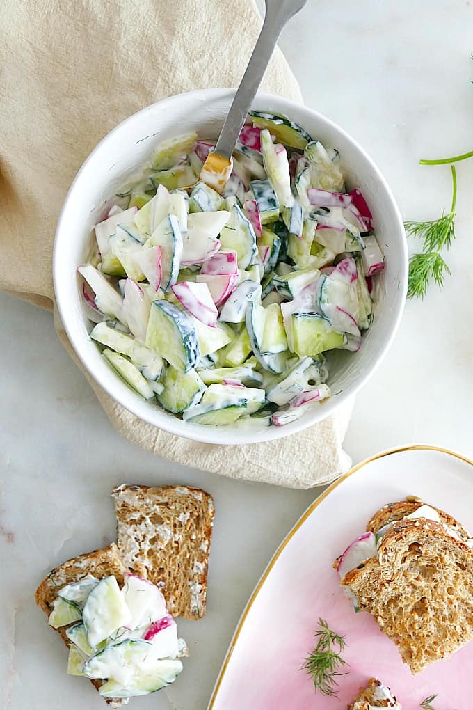 white bowl with sliced cucumbers and radishes mixed with dill cream cheese