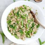 Snap pea, quinoa, and chickpea salad in a bowl with a wooden spoon.