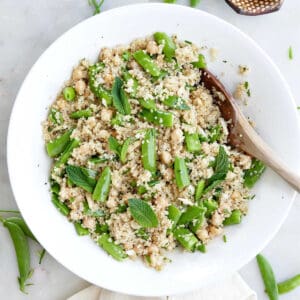 Snap pea, quinoa, and chickpea salad in a bowl with a wooden spoon.